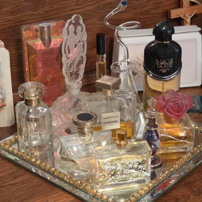 Sale Photo Thumbnail #186: Collection of vintage and designer perfume bottles displayed on a mirror vanity tray, including Lancôme Magie Noire, Chanel Gabrielle, and Bvlgari.