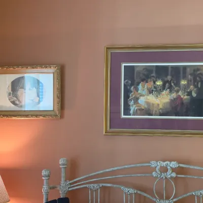 Sale Photo Thumbnail #110: Two framed traditional art prints hanging on a peach wall above a white wrought iron bed frame.