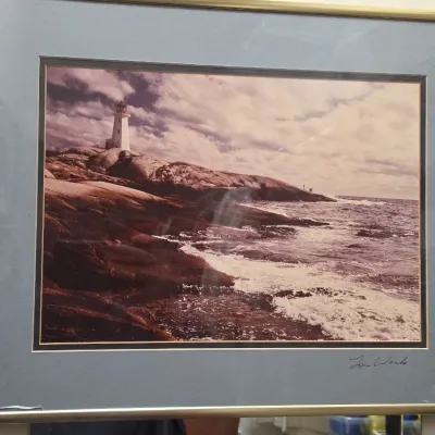 Sale Photo Thumbnail #156: Framed coastal photograph depicting Peggy's Cove lighthouse, signed by the artist on the matting and presented in a thin metal gold-tone frame.