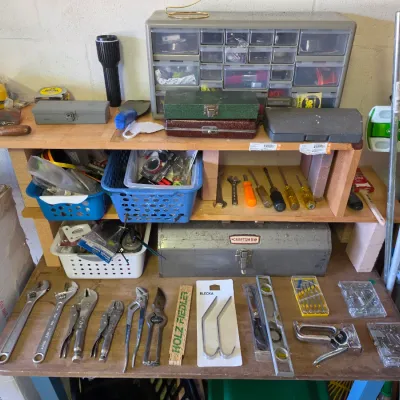 Sale Photo Thumbnail #279: Wooden workbench arranged with various hand tools, including adjustable wrenches, locking pliers, screwdrivers, a Craftsman metal toolbox, and a multi-drawer hardware organizer.