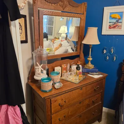 Sale Photo Thumbnail #185: Antique carved oak dresser with attached mirror, displaying perfume bottles, candles, and decorative glass jars on its surface.