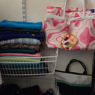 Sale Photo Thumbnail #162: Pink and white patterned tote bag hanging beside a wire closet basket filled with folded scarves and textiles.