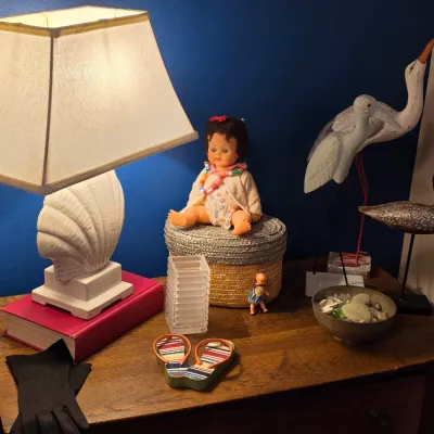 Sale Photo Thumbnail #180: Vintage white ceramic seashell table lamp paired with coastal decor items, including bird figurines, a vintage baby doll, and decorative accents arranged on a wooden dresser.