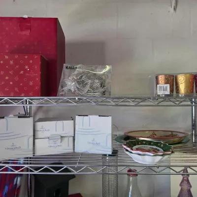 Sale Photo Thumbnail #276: Selection of boxed Christmas decor, including Villeroy & Boch items, decorative votive candle holders, and holiday serving dishes displayed on a wire shelf.