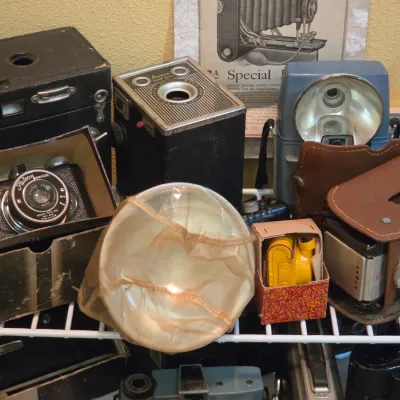 Sale Photo Thumbnail #207: Collection of vintage cameras and accessories, including Ansco and Falcon box cameras, flash attachments, and protective leather cases, mid-20th century.