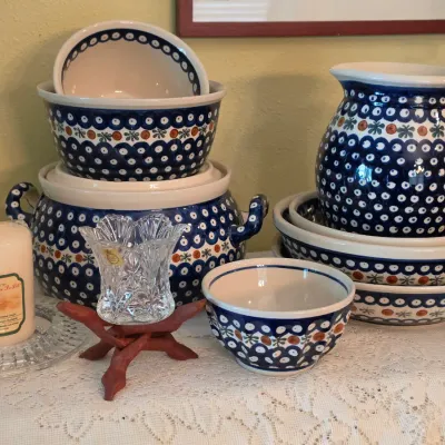 Sale Photo Thumbnail #80: Collection of Polish pottery Bolesławiec stoneware, featuring peacock eye pattern bowls, a pitcher, and a covered casserole dish alongside cut crystal decorative items.