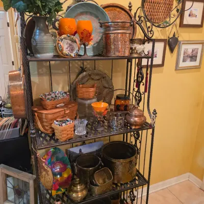Sale Photo Thumbnail #57: Black wrought iron baker's rack filled with various home decor items, including woven Longaberger-style baskets, copper vessels, pottery, and art pieces.