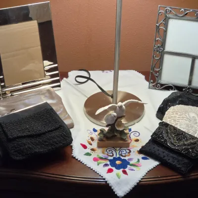 Sale Photo Thumbnail #146: Collection of vintage evening bags and clutch purses displayed alongside picture frames, an embroidered cloth, and a bird figurine lamp base.
