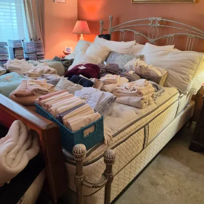 Sale Photo Thumbnail #107: Large collection of folded linens, towels, and bedding arranged on a distressed metal queen or king bed frame.