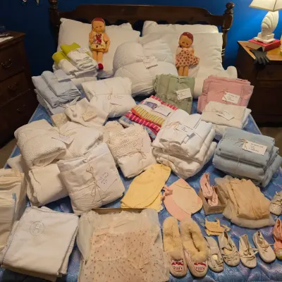 Sale Photo Thumbnail #183: Large collection of vintage linens, bedsheets, blankets, dolls, baby clothes, and baby shoes displayed on a wooden bed frame.