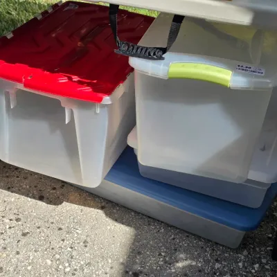 Sale Photo Thumbnail #338: Selection of clear plastic storage totes with red, green, and blue lids, shown stacked under a folding table.