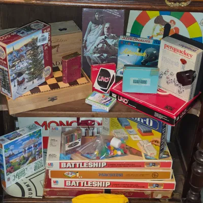 Sale Photo Thumbnail #172: Collection of vintage board games, card games, and jigsaw puzzles, including Battleship, Monopoly, Uno, and Perquackey, arranged on a wooden shelf.