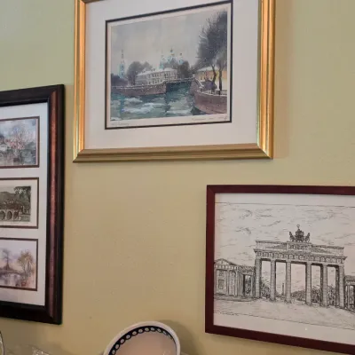 Sale Photo Thumbnail #78: Collection of framed artwork featuring European architectural and city views, including a pen-and-ink drawing of the Brandenburg Gate and matted watercolor prints.