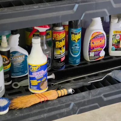 Sale Photo Thumbnail #284: Assortment of household and garden chemicals, including Zep, Raid, Purple Power, and Organocide, alongside cleaning tools on a black plastic utility shelf.
