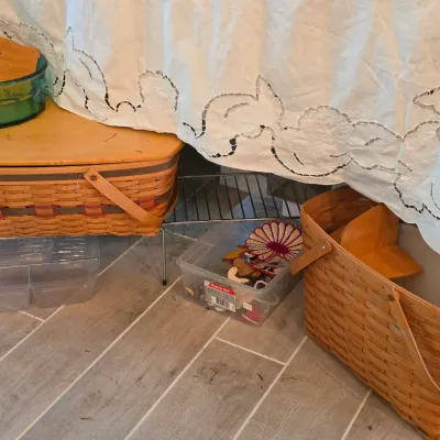 Sale Photo Thumbnail #83: Selection of vintage woven picnic baskets, clear plastic storage containers, a teal glass bowl, and embroidered linens stored under a table.