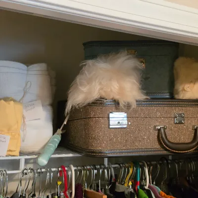 Sale Photo Thumbnail #200: Vintage luggage pieces resting on a closet shelf alongside folded linens and various accessories.