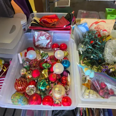 Sale Photo Thumbnail #316: Clear plastic storage bins filled with vintage and modern Christmas decorations, including colorful glass baubles, string lights, and holiday art.