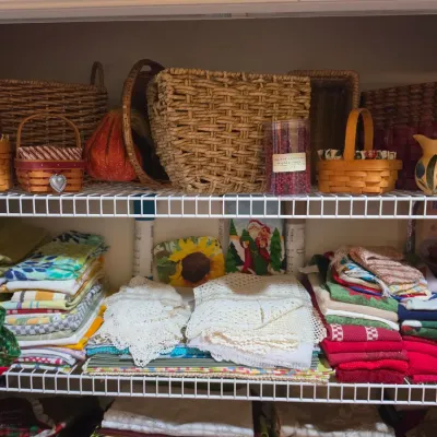 Sale Photo Thumbnail #66: Wire closet shelves filled with woven storage baskets, Longaberger style wooden baskets, decorative ceramics, and neatly stacked linens and lace doilies.