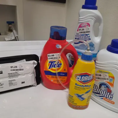 Sale Photo Thumbnail #265: Assortment of laundry and cleaning supplies including Tide detergent, Woolite detergent, Clorox ReadyMop floor cleaner, and Kirkland wipes.