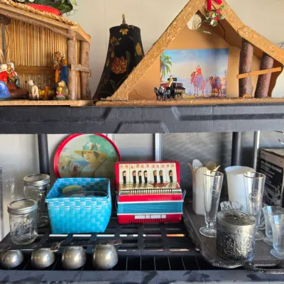 Sale Photo Thumbnail #305: Black plastic shelving unit holding miscellaneous collectibles, including nativity stables, a vintage toy accordion, glassware, Ball jars, and home decor items.