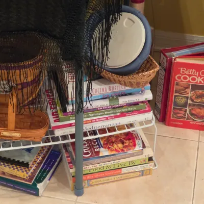 Sale Photo Thumbnail #42: Collection of vintage and modern cookbooks alongside woven baskets arranged on a low white wire rack.