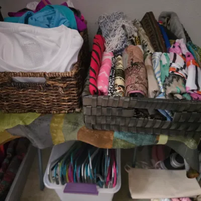 Sale Photo Thumbnail #163: Woven storage baskets filled with folded clothing and colorful scarves, arranged alongside plastic clothes hangers in a bin.