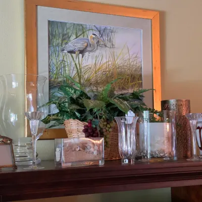 Sale Photo Thumbnail #86: Framed heron art print mounted above a collection of home decor, including glass vases, a shell display box, and small picture frames.