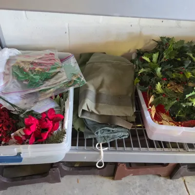 Sale Photo Thumbnail #302: Selection of holiday decor items including artificial greenery, red floral picks, and craft supplies stored in clear plastic bins alongside folded green textiles.