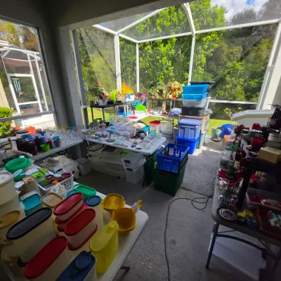 Sale Photo Thumbnail #319: Outdoor screened patio displaying folding tables filled with vintage Tupperware, glassware, small appliances, and plastic storage totes.