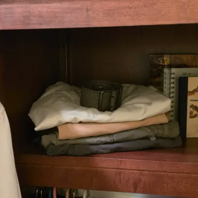 Sale Photo Thumbnail #255: Stack of folded pants topped with a canvas webbed belt inside a wooden closet cubby, alongside spiral notebooks.