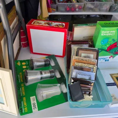 Sale Photo Thumbnail #310: Assortment of household items including various picture frames, packaged LED lanterns, and boxed vintage Christmas tree stands.