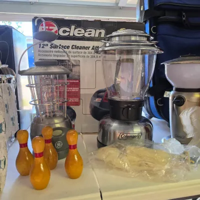 Sale Photo Thumbnail #313: Selection of table items including Coleman battery-powered lanterns, small wooden bowling pins, and an EZ Clean surface cleaner accessory box.