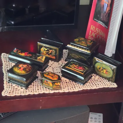 Sale Photo Thumbnail #90: Collection of hand-painted Russian lacquer trinket boxes with detailed folklore scenes, displayed alongside a Russian art book.