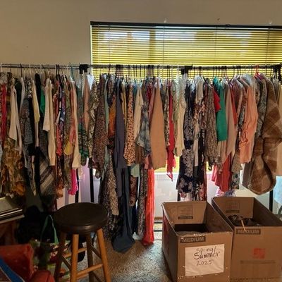 Sale Photo Thumbnail #10: Clothing rack filled with women's colorful garments alongside cardboard storage boxes and a wooden stool.