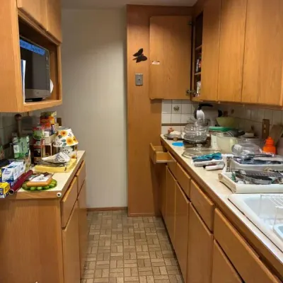 Sale Photo Thumbnail #15: Narrow galley kitchen featuring mid-century style honey-oak cabinets filled with assorted household items, kitchenware, and small appliances.