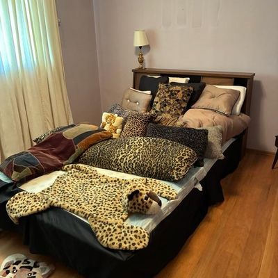 Sale Photo Thumbnail #2: Bedroom set featuring a wooden headboard, mattress, and an assortment of animal print and textured throw pillows and novelty plush rugs.