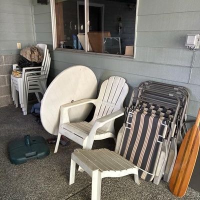 Sale Photo Thumbnail #5: Collection of outdoor patio items, including plastic resin Adirondack and stackable chairs, folding lawn chairs, a round table top, umbrella base, and a wooden canoe paddle.