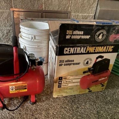 Sale Photo Thumbnail #4: Central Pneumatic 3-gallon oilless air compressor, shown next to its original cardboard box with stacked plastic buckets in the background.