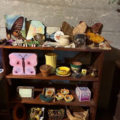 Sale Photo Thumbnail #7: Wooden four-tier display shelf filled with butterfly and sunflower-themed home decor items, planters, small figurines, and framed artwork.