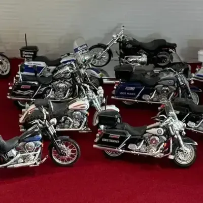 Collection of die-cast toy motorcycle models, featuring various police and cruiser styles, displayed on a red surface.