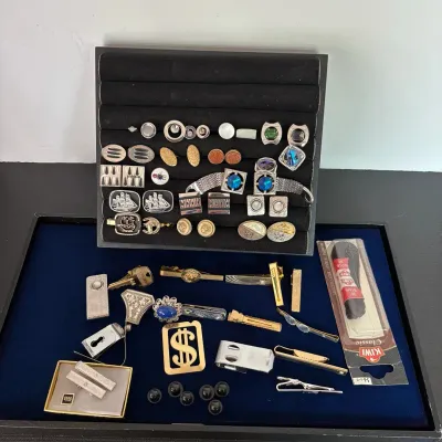 Collection of vintage men's accessories including cufflinks, tie clips, money clips, and lapel pins displayed in velvet trays.