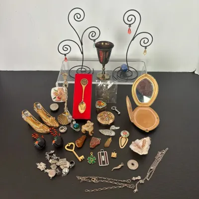 Assortment of vintage trinkets and jewelry, including miniature decorative shoes, compacts, pendants, metal spoons, and wire jewelry stands.