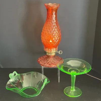 Vintage orange diamond-quilted pattern glass hurricane lamp alongside two green depression glass serving pieces.