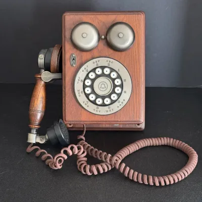 Vintage-style wall-mount telephone with a oak-look wooden body, brass bells, push-button dial formatted like a rotary face, and attached...