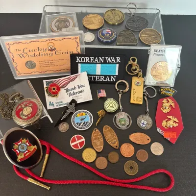 Collection of military and souvenir collectibles including commemorative coins, lapel pins, keychains, a Korean War Veteran patch, and a...