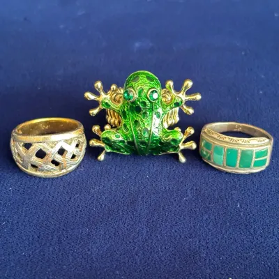 Collection of three costume rings featuring a green enameled frog statement ring flanked by a gold-tone lattice band and a green stone...