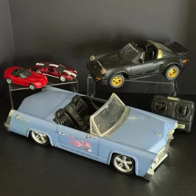 Collection of toy and remote-controlled cars, including a light blue vintage-style convertible with flame decals, a black Porsche...