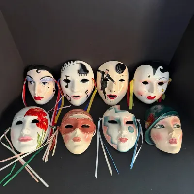 Collection of eight ceramic decorative face masks featuring various painted artistic designs, Art Deco influences, and ribbon accents.