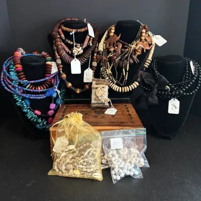 Collection of bohemian and statement beaded necklaces displayed on jewelry busts alongside a wood decorative box and bagged shell jewelry.