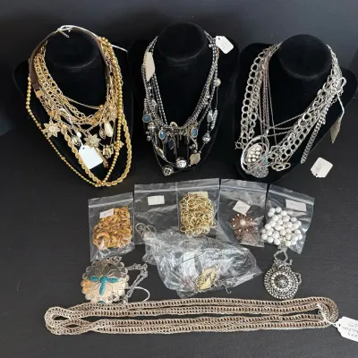 Collection of vintage fashion jewelry, featuring layered statement necklaces displayed on black busts alongside individually bagged...